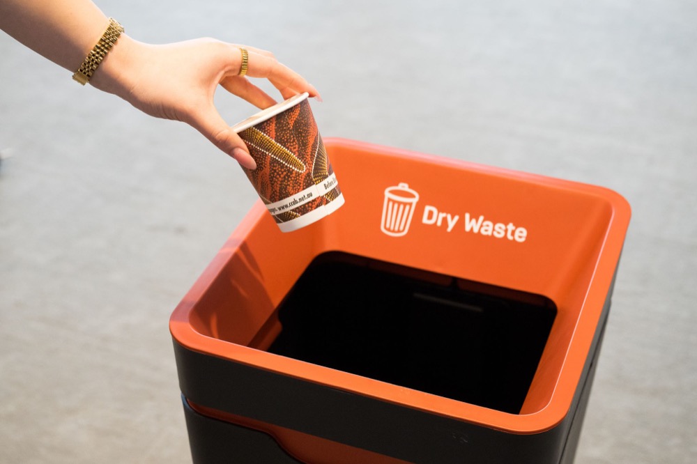 A hand placing a cup into a dry waste recycling bin at Parramatta Square